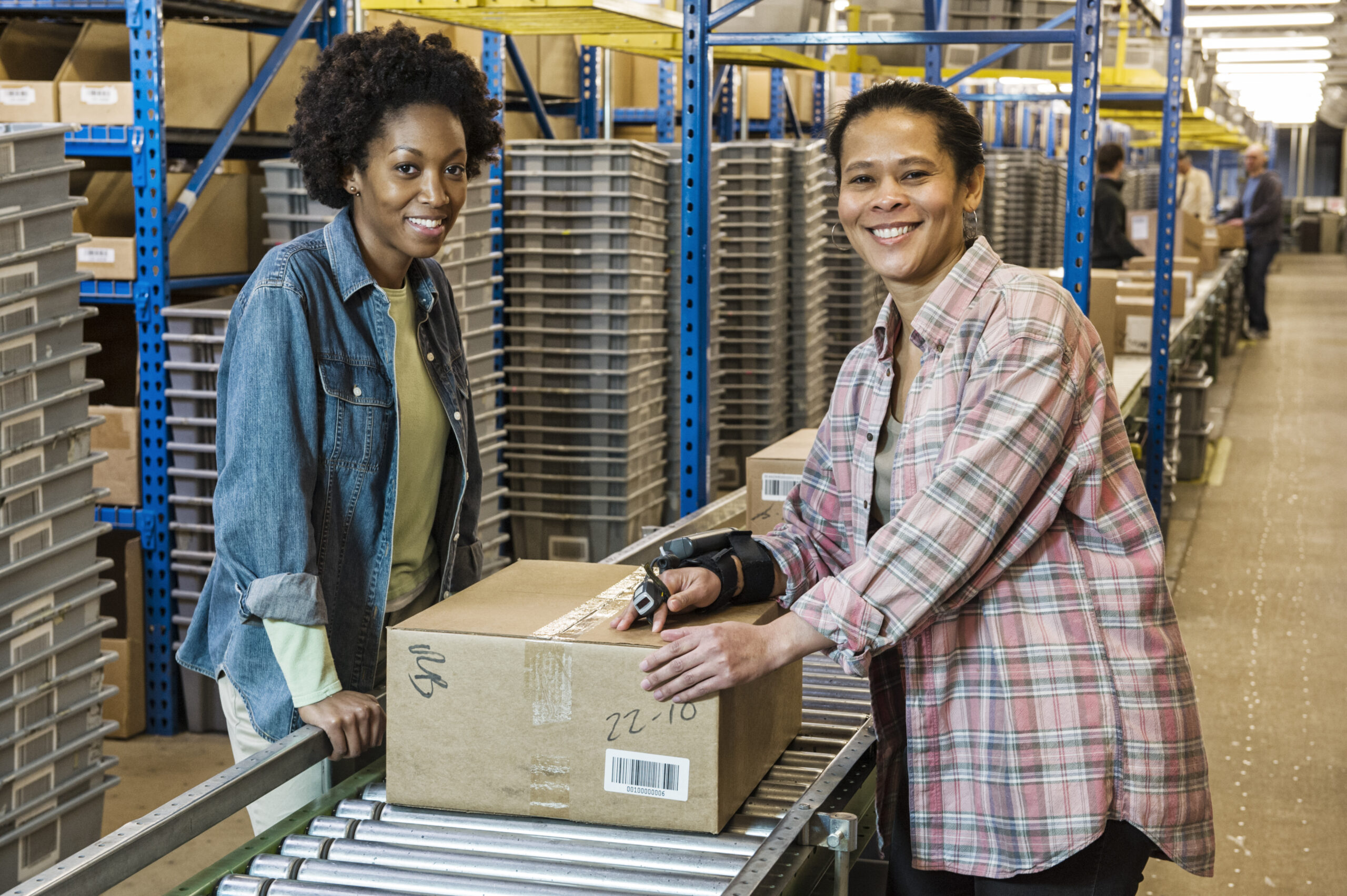 Team portrait of multi-ethnic female warehouse workers working next to a motorzied feed conveyor in a large distribution warehouse.